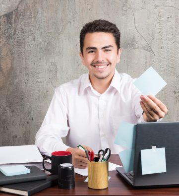 Office employee happily showing his memo pad at the office desk. High quality photo